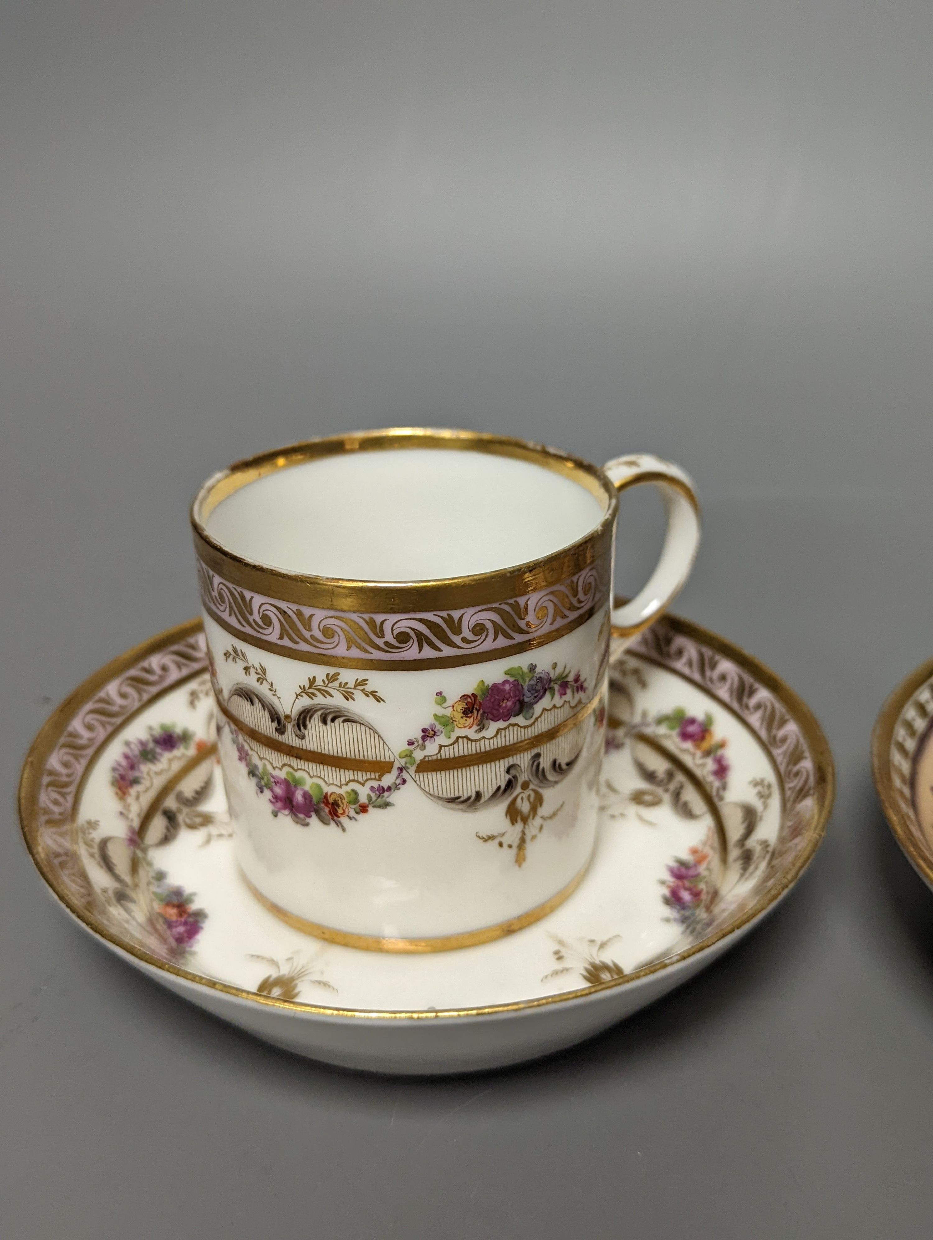 A Duc d'Angouleme coffee can and saucer painted with a puce chain of leaves on a salmon coloured ground and another painted with a flower chain, black feather and a gilt line, latter with stencilled red mark 'Manuf de M